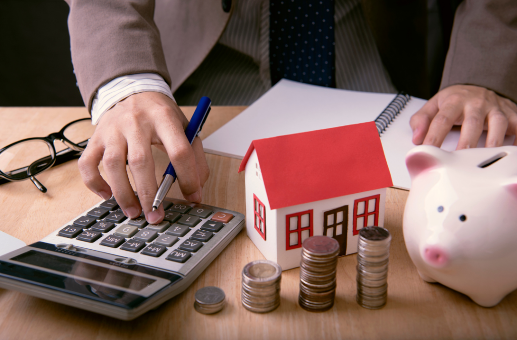 A property manager calculating finances with a model house, coins, and piggy bank, illustrating how to set the best price for rental property.