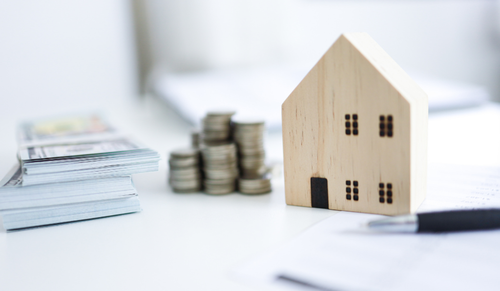 Wooden house model with stacks of coins and documents, representing financial management through cloud-based software for property management.
