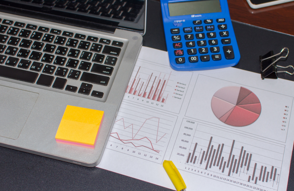 A laptop and graphs alongside a calculator, showcasing data analysis for how to set the best price for rental property.
