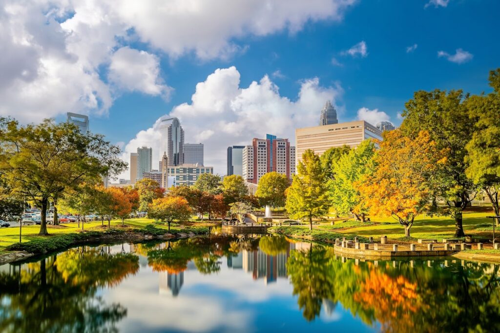 A stunning travel destination in Charlotte, North Carolina, featuring the city skyline reflected in a serene park lake with autumn foliage.